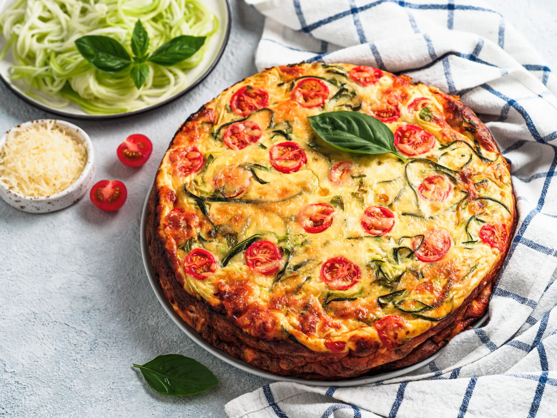 Torta salata fit con zucchine, pomodorini e basilico fresco, servita su un piatto.