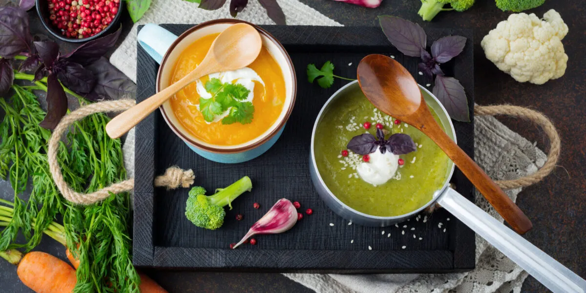 Due vellutate fit, una arancione e una verde, servite con yogurt ed erbe aromatiche, circondate da carote, broccoli, cavolfiore e spezie.