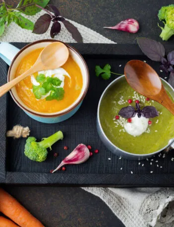 Due vellutate fit, una arancione e una verde, servite con yogurt ed erbe aromatiche, circondate da carote, broccoli, cavolfiore e spezie.