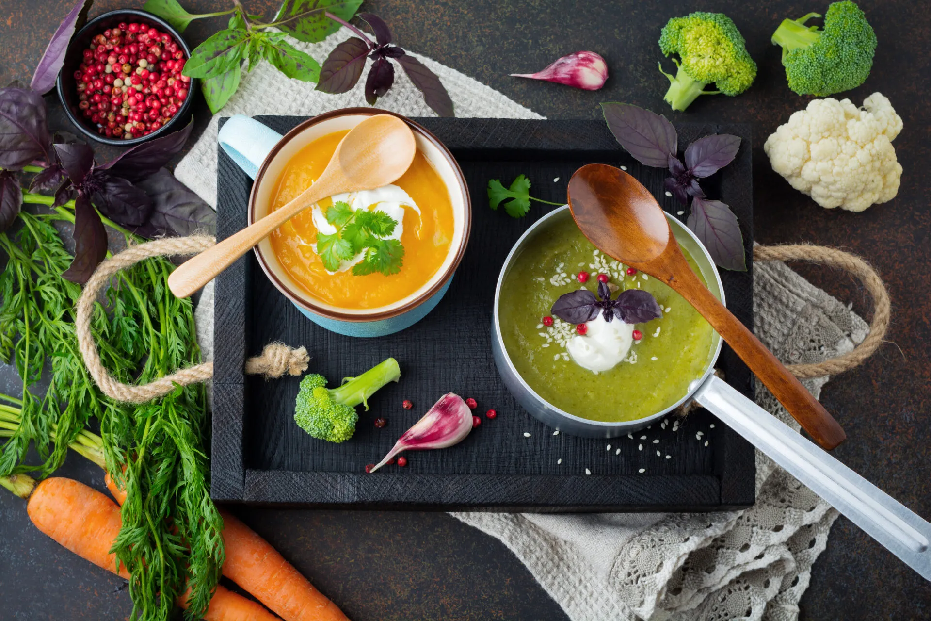 Due vellutate fit, una arancione e una verde, servite con yogurt ed erbe aromatiche, circondate da carote, broccoli, cavolfiore e spezie.