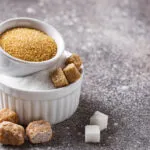 Ciotole con zucchero bianco e zucchero di canna, con zollette sparse su un piano grigio