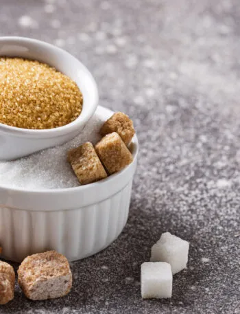 Ciotole con zucchero bianco e zucchero di canna, con zollette sparse su un piano grigio