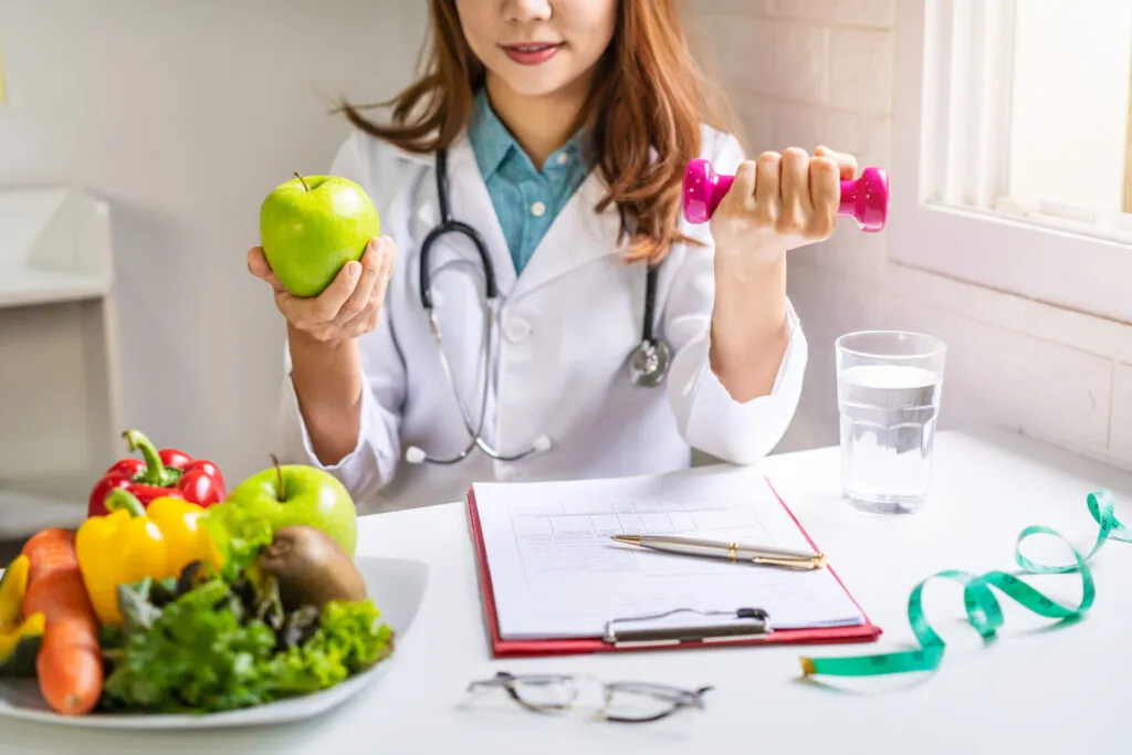 Dietista mostra una mela e un piccolo peso durante una consulenza su alimentazione equilibrata e gestione della fame nervosa.