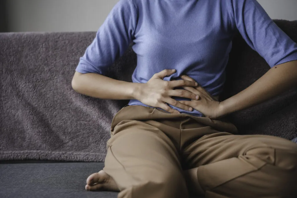 Persona seduta con le mani sull'addome a causa di una digestione lenta e di un fastidio addominale, sintomi spesso associati a gonfiore e cattiva digestione.