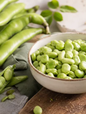 Fave fresche sgranate in ciotola con baccelli verdi