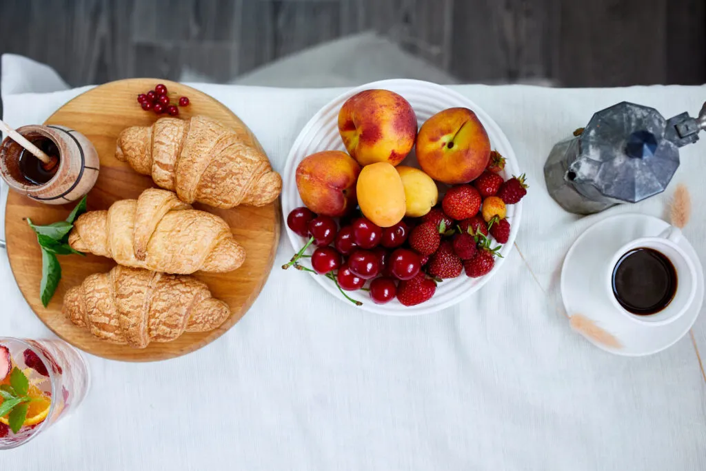 Ciotola di frutta fresca accanto a cornetti e caffè, esempio di frutta consumata a colazione come parte di un'alimentazione equilibrata.