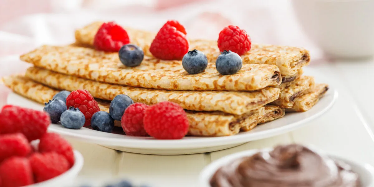Crêpes dorate piegate con lamponi e mirtilli su piatto bianco