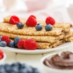 Crêpes dorate piegate con lamponi e mirtilli su piatto bianco
