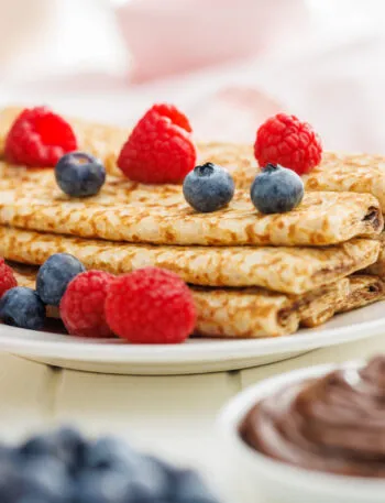 Crêpes dorate piegate con lamponi e mirtilli su piatto bianco