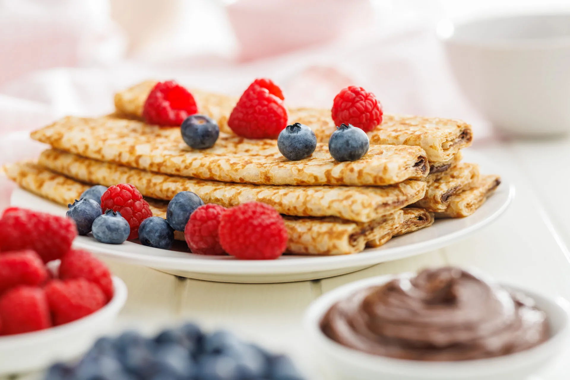 Crêpes dorate piegate con lamponi e mirtilli su piatto bianco