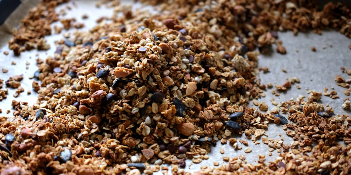 Granola fatta in casa con fiocchi d’avena, frutta secca, semi e gocce di cioccolato su una teglia.