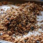 Granola fatta in casa con fiocchi d’avena, frutta secca, semi e gocce di cioccolato su una teglia.