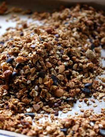 Granola fatta in casa con fiocchi d’avena, frutta secca, semi e gocce di cioccolato su una teglia.