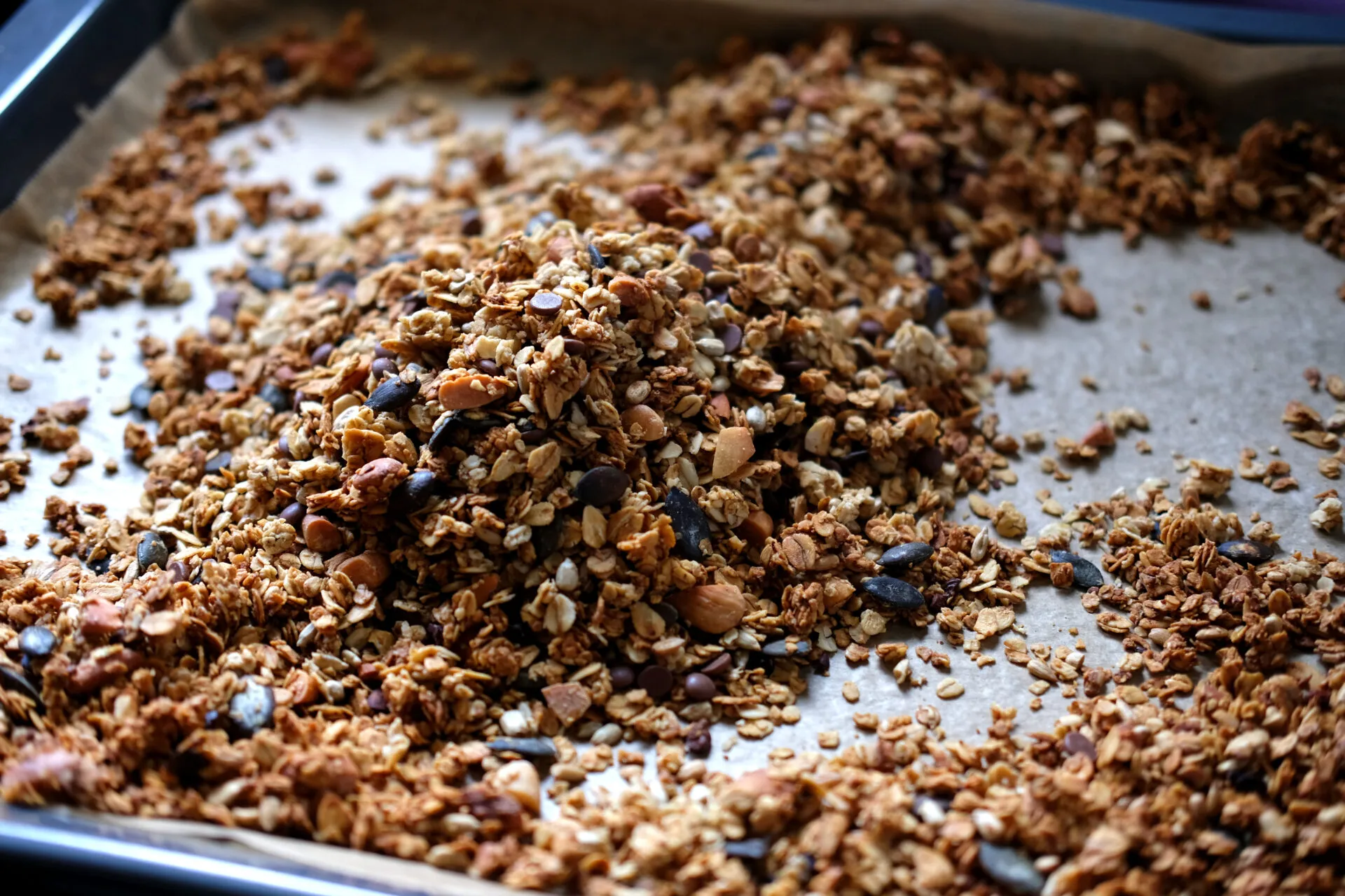 Granola fatta in casa con fiocchi d’avena, frutta secca, semi e gocce di cioccolato su una teglia.