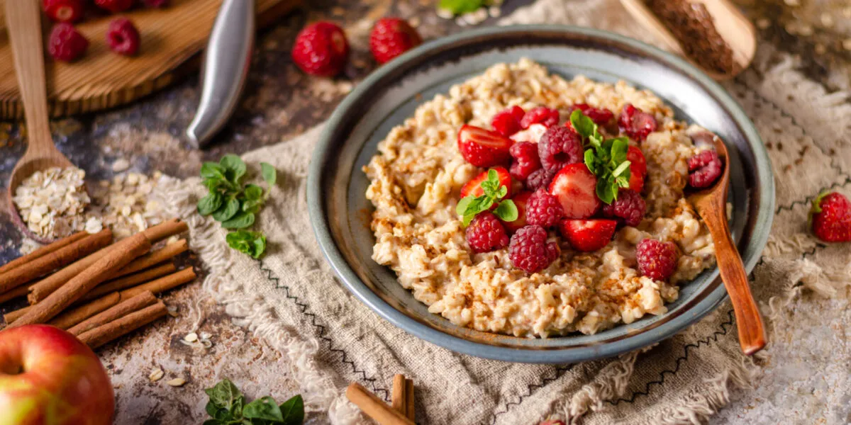 Overnight oats cremosi con fragole, lamponi, cannella e foglie di menta serviti in una ciotola.