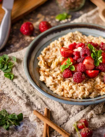 Overnight oats cremosi con fragole, lamponi, cannella e foglie di menta serviti in una ciotola.