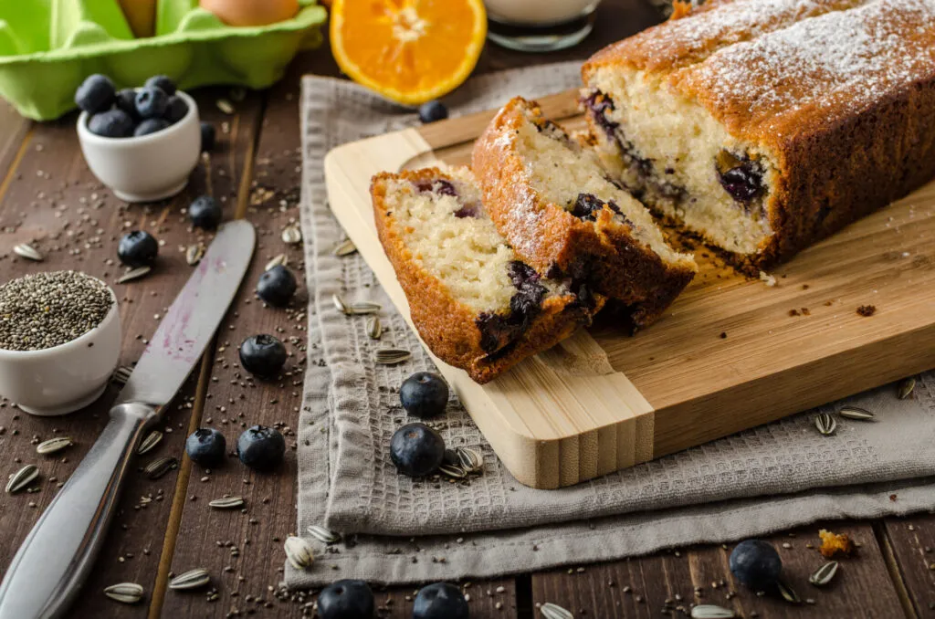 Plumcake fit ai mirtilli tagliato a fette e spolverato con zucchero a velo su un tagliere di legno.