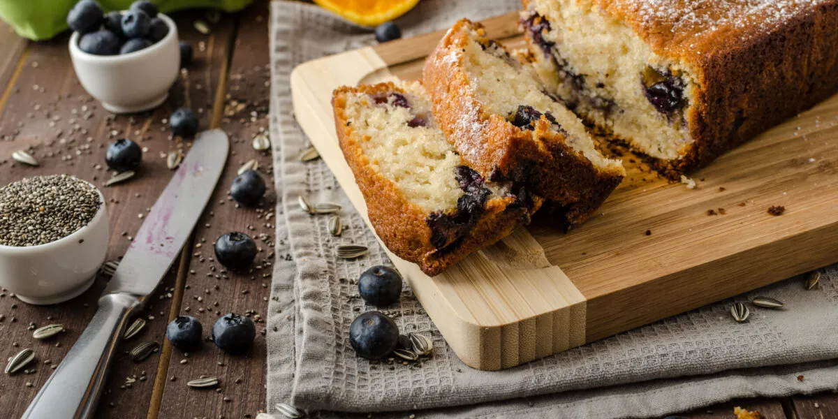 Plumcake fit ai mirtilli tagliato a fette e spolverato con zucchero a velo su un tagliere di legno.