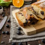 Plumcake fit ai mirtilli tagliato a fette e spolverato con zucchero a velo su un tagliere di legno.
