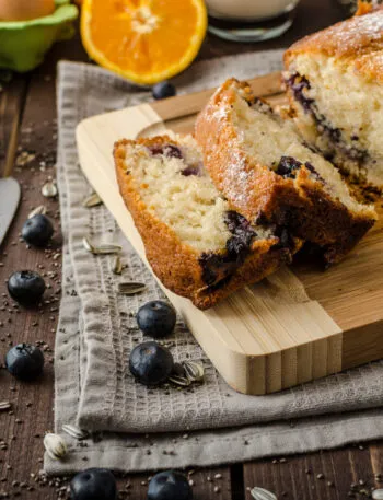 Plumcake fit ai mirtilli tagliato a fette e spolverato con zucchero a velo su un tagliere di legno.