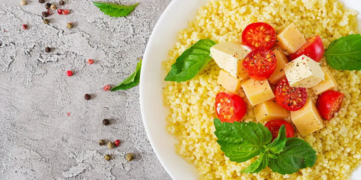 Piatto di cous cous con pomodorini, cubetti di formaggio, basilico fresco e pepe.