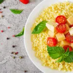 Piatto di cous cous con pomodorini, cubetti di formaggio, basilico fresco e pepe.