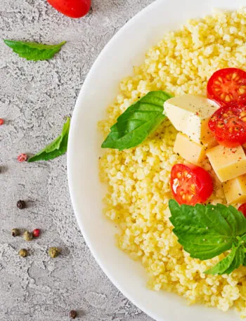 Piatto di cous cous con pomodorini, cubetti di formaggio, basilico fresco e pepe.