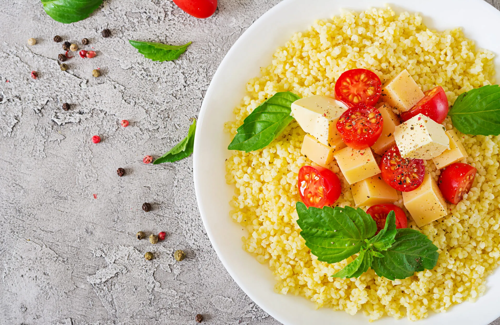 Piatto di cous cous con pomodorini, cubetti di formaggio, basilico fresco e pepe.