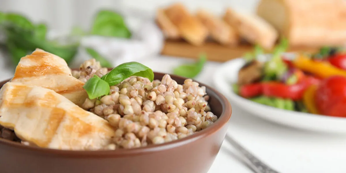 Ciotola di farro con pollo grigliato e basilico, accompagnata da verdure fresche.