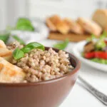 Ciotola di farro con pollo grigliato e basilico, accompagnata da verdure fresche.