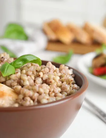 Ciotola di farro con pollo grigliato e basilico, accompagnata da verdure fresche.