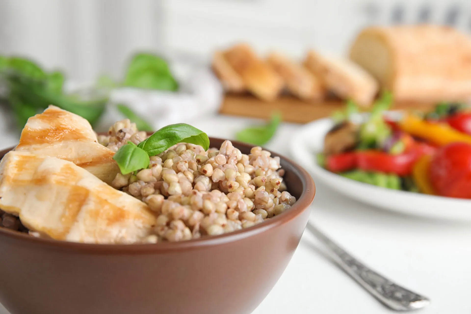 Ciotola di farro con pollo grigliato e basilico, accompagnata da verdure fresche.