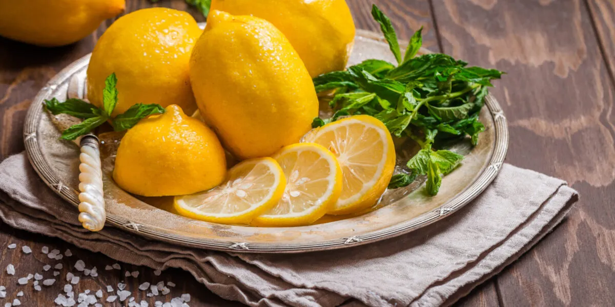 Limoni interi e a fette con menta fresca su piatto di metallo e tavolo di legno