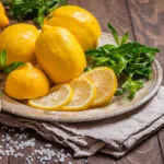 Limoni interi e a fette con menta fresca su piatto di metallo e tavolo di legno