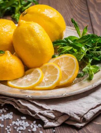 Limoni interi e a fette con menta fresca su piatto di metallo e tavolo di legno