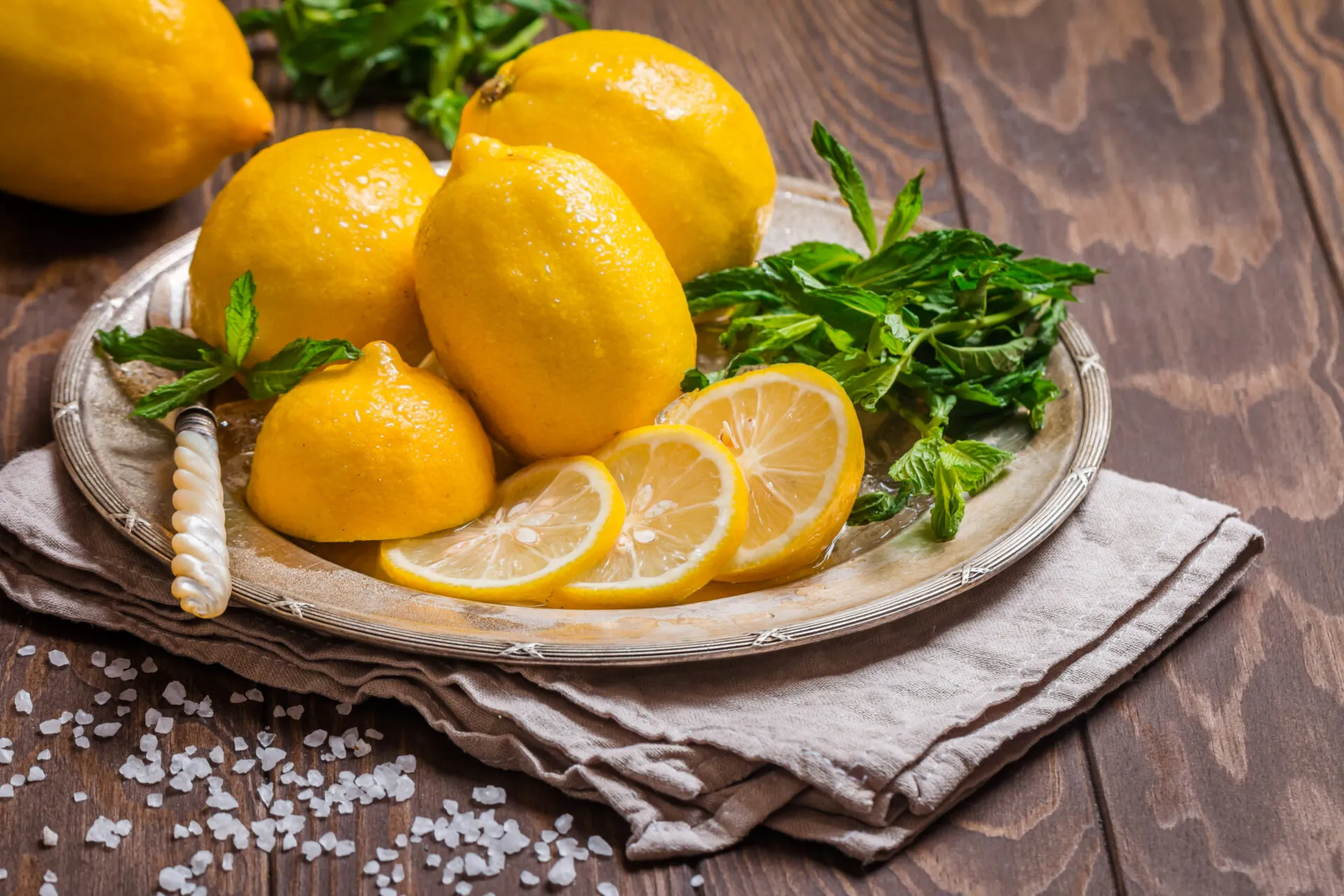 Limoni interi e a fette con menta fresca su piatto di metallo e tavolo di legno