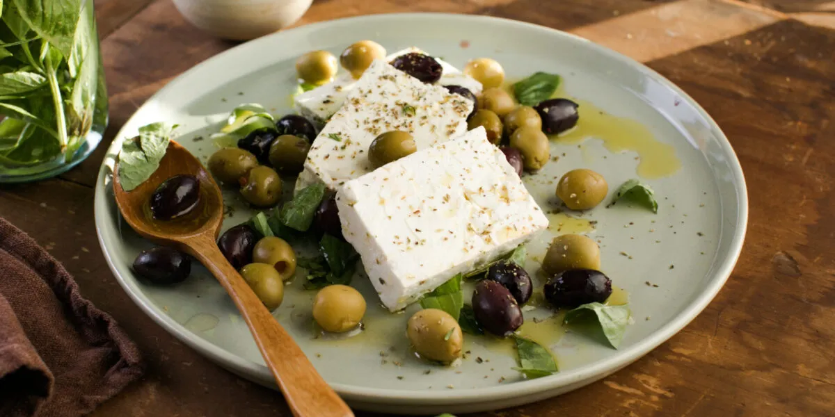 Feta con olive verdi e nere, basilico fresco, olio ed erbe aromatiche su un piatto.
