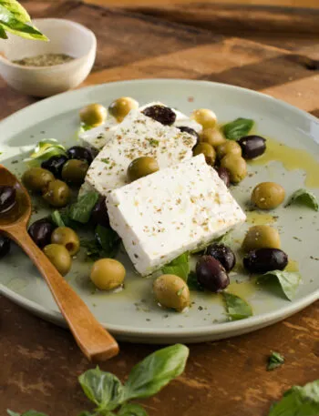 Feta con olive verdi e nere, basilico fresco, olio ed erbe aromatiche su un piatto.