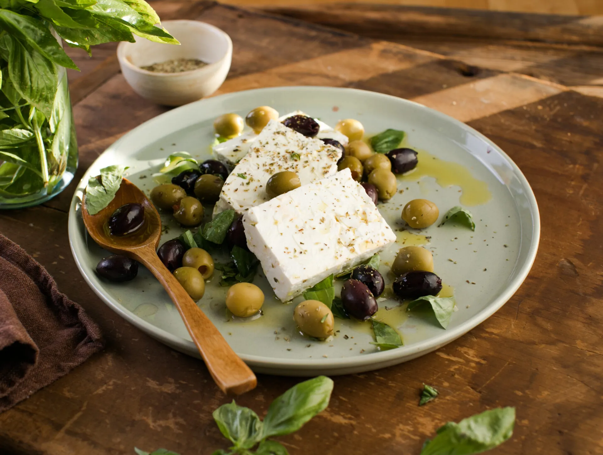 Feta con olive verdi e nere, basilico fresco, olio ed erbe aromatiche su un piatto.
