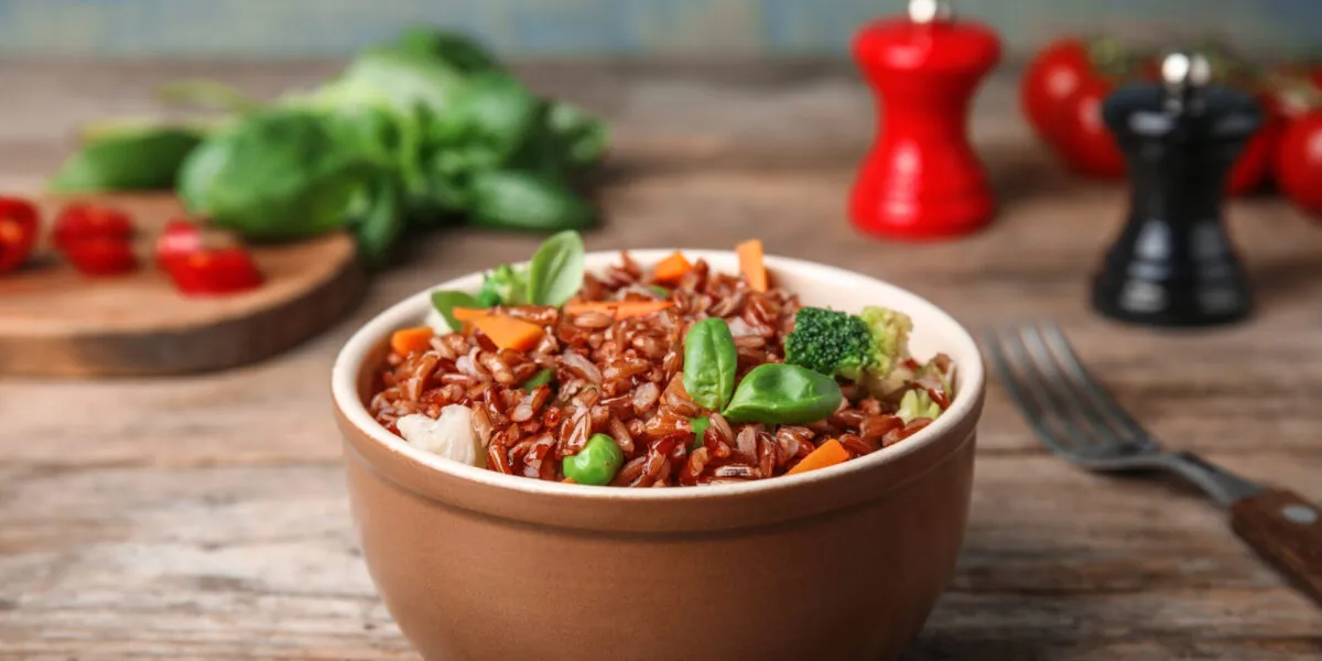 Bowl di riso integrale con broccoli, carote, piselli e foglie di basilico.