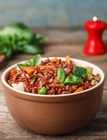 Bowl di riso integrale con broccoli, carote, piselli e foglie di basilico.