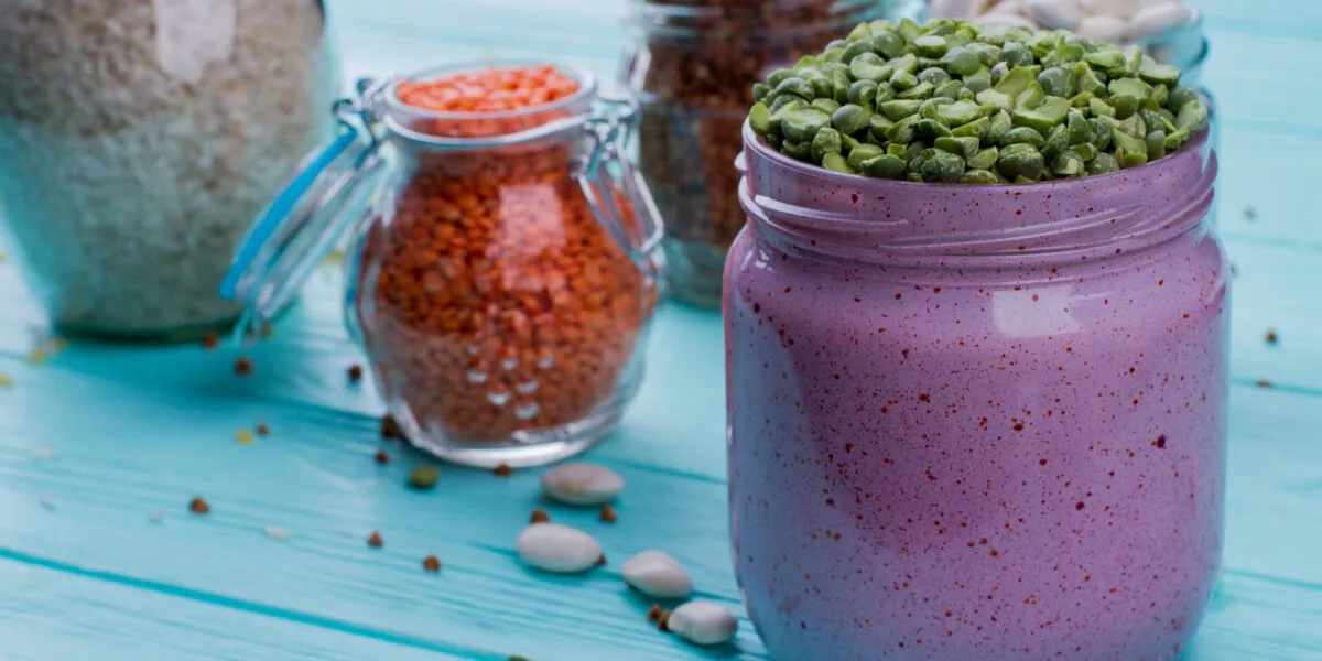 Smoothie proteico viola in barattolo con legumi, cereali e ingredienti secchi sullo sfondo.