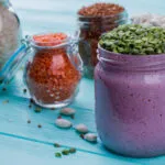 Smoothie proteico viola in barattolo con legumi, cereali e ingredienti secchi sullo sfondo.