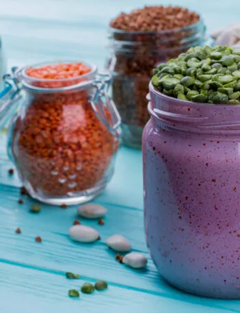 Smoothie proteico viola in barattolo con legumi, cereali e ingredienti secchi sullo sfondo.