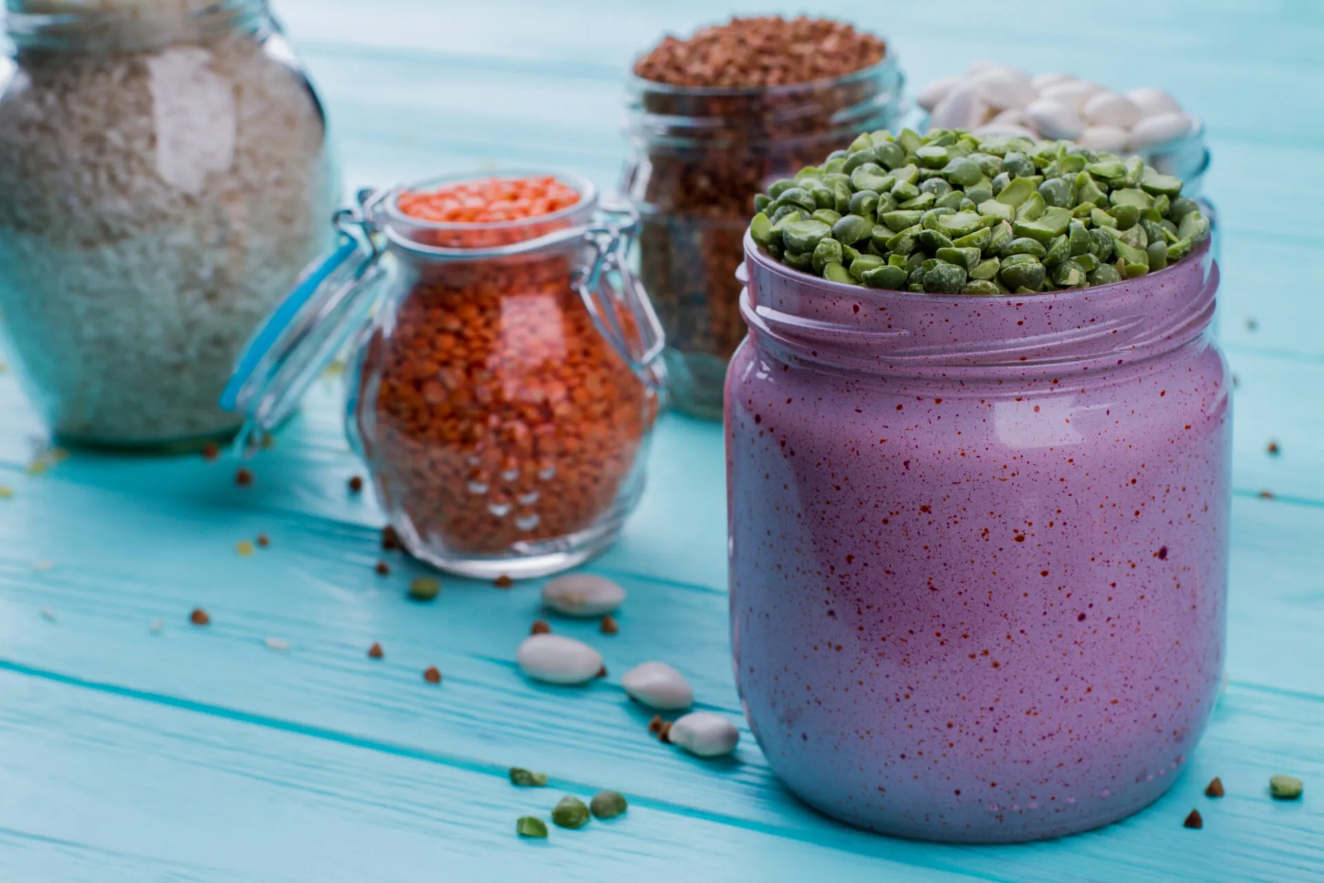 Smoothie proteico viola in barattolo con legumi, cereali e ingredienti secchi sullo sfondo.