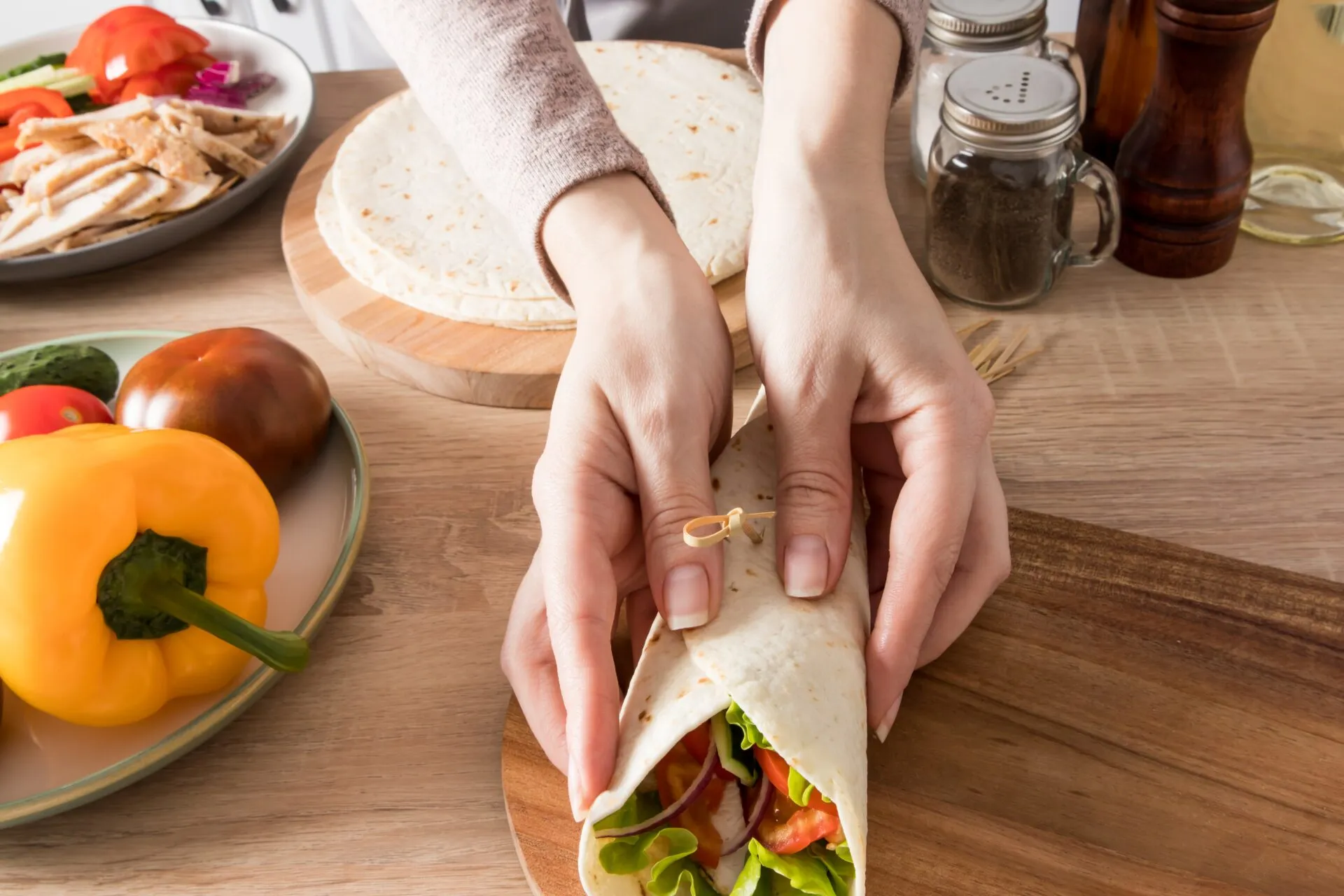 Mani che chiudono un wrap fit ripieno di pollo, lattuga, pomodoro, cetriolo e cipolla rossa.
