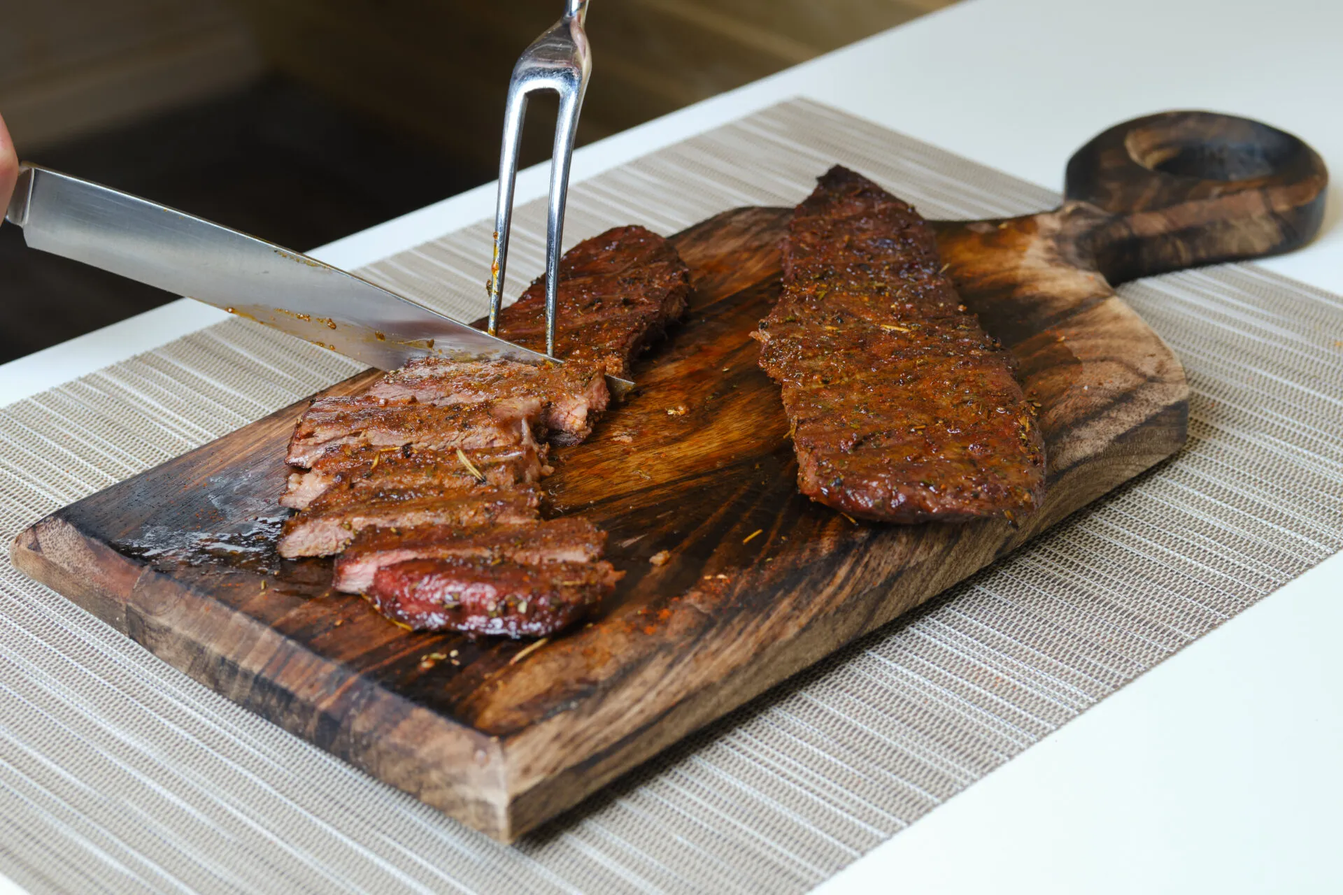 Carne affumicata con crosta di erbe affettata su un tagliere di legno con coltello e forchettone
