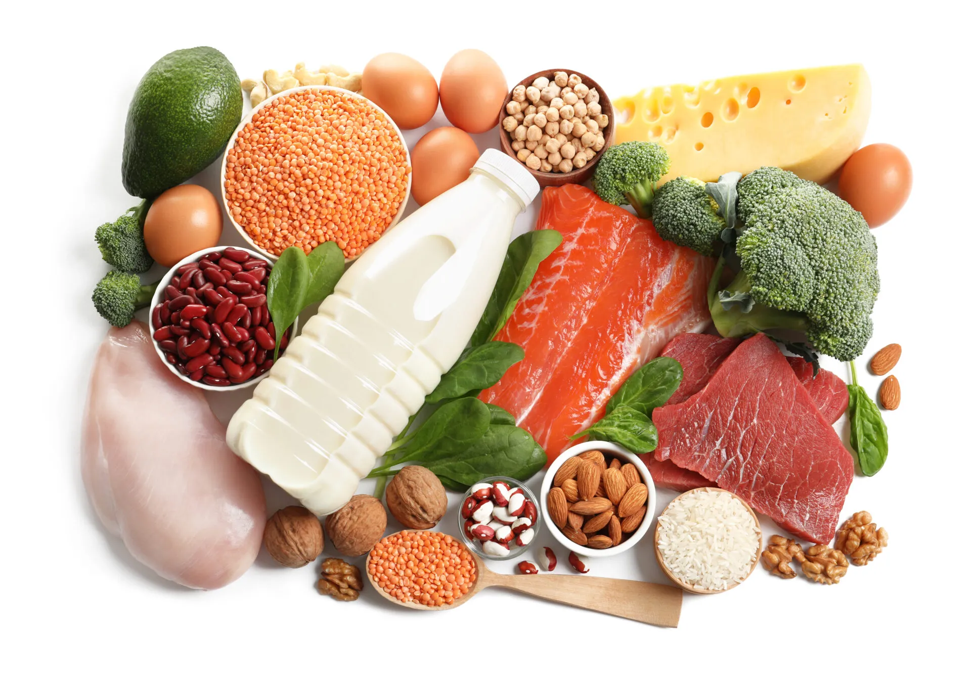 Vista dall’alto di fonti proteiche diverse su fondo bianco: petto di pollo, salmone, uova, legumi, formaggio, frutta secca, riso e broccoli
