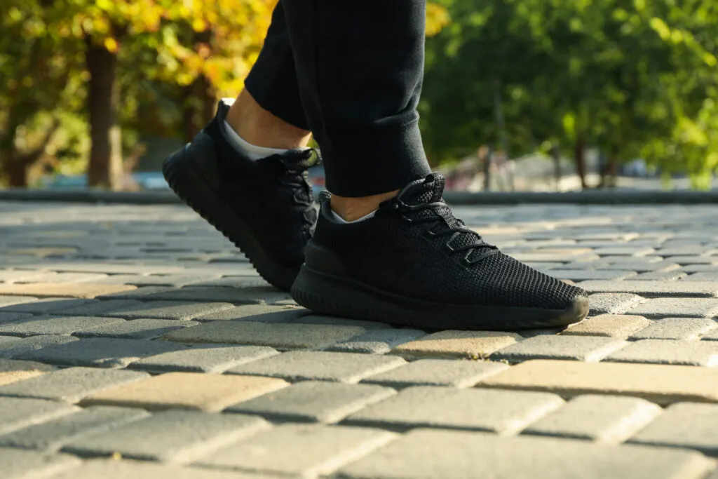 Primo piano di scarpe da ginnastica nere in movimento su un vialetto pavimentato, con alberi verdi sullo sfondo