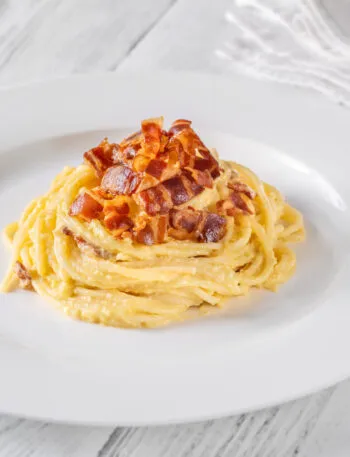 Piatto di spaghetti alla carbonara con crema liscia e lucida che avvolge la pasta, con guanciale croccante sopra